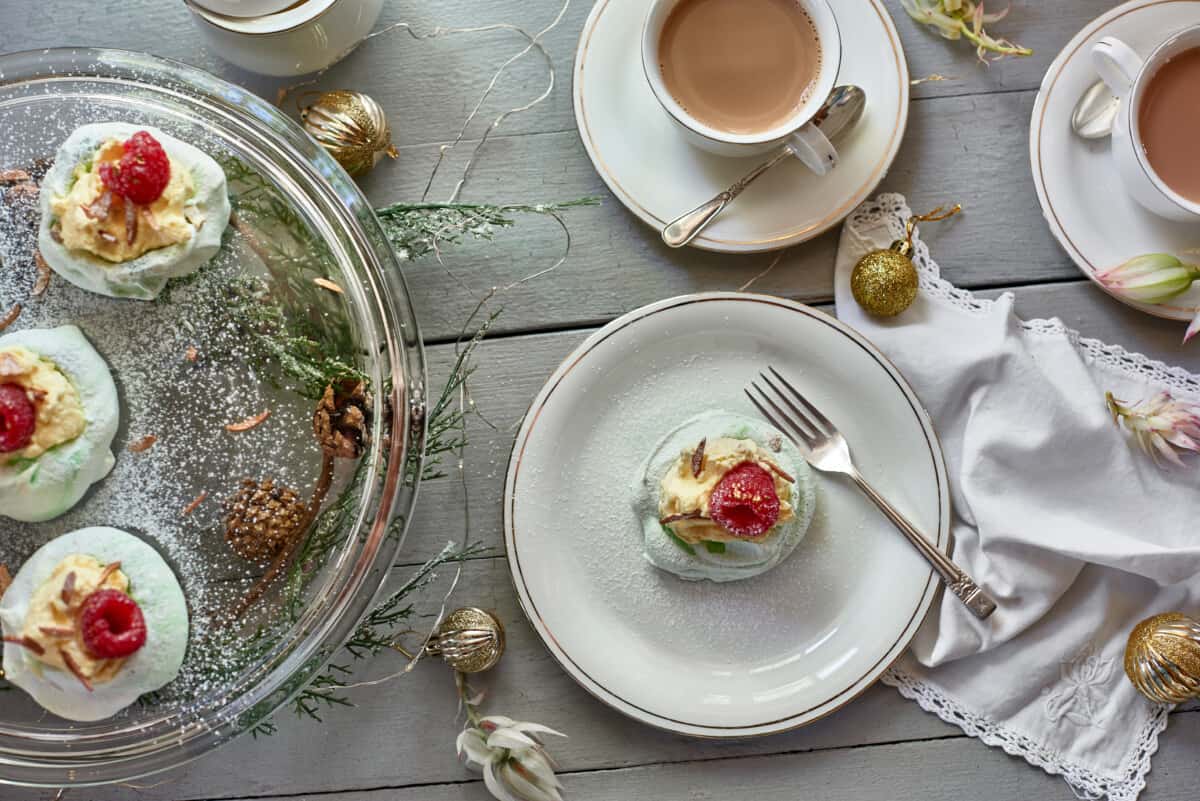 Mini pistachio and raspberry pavlova on small white plate with fork placed next to a cup of tea.