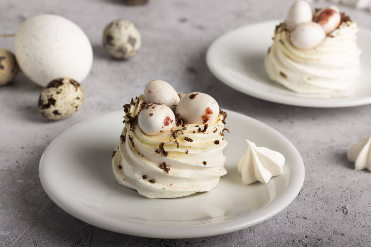 Mini pavlova topped with whipped cream and three small candy coated chocolates, sprinkled with dark chocolate shavings