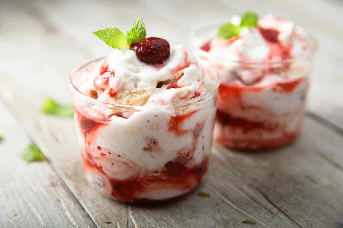 Two raspberry pavlova trifle verrine. Layers of pavlova, rqspberry coulis and whipped cream, topped with a fresh raspberry and mint leaf for decoration.