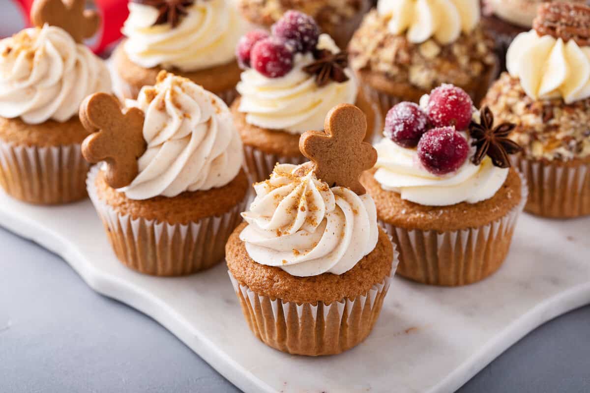 Vanilla cupcakes with gingerbread frosting, a Christmas tea party menu item, served on a platter. Cupcakes are decorated with gingerbread men and berries.