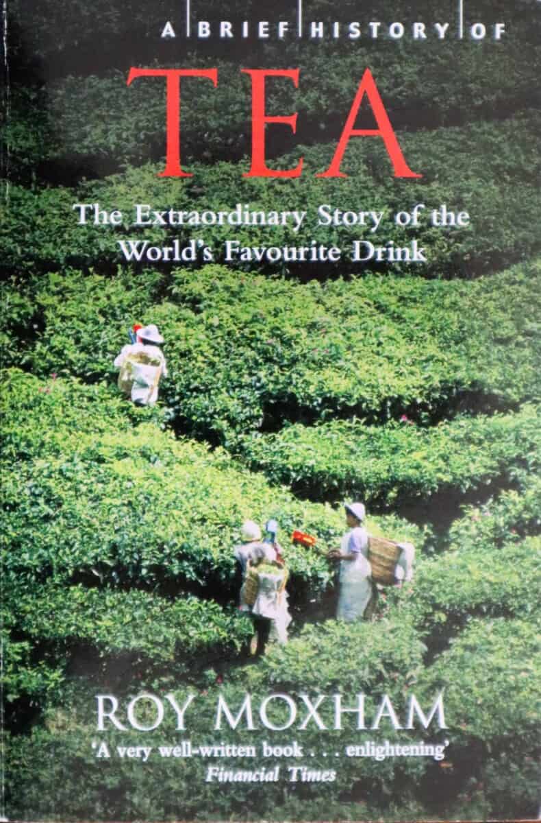 Cover of "a brief history of tea" by Roy Moxham shoing three people walking up a path in a tea field.