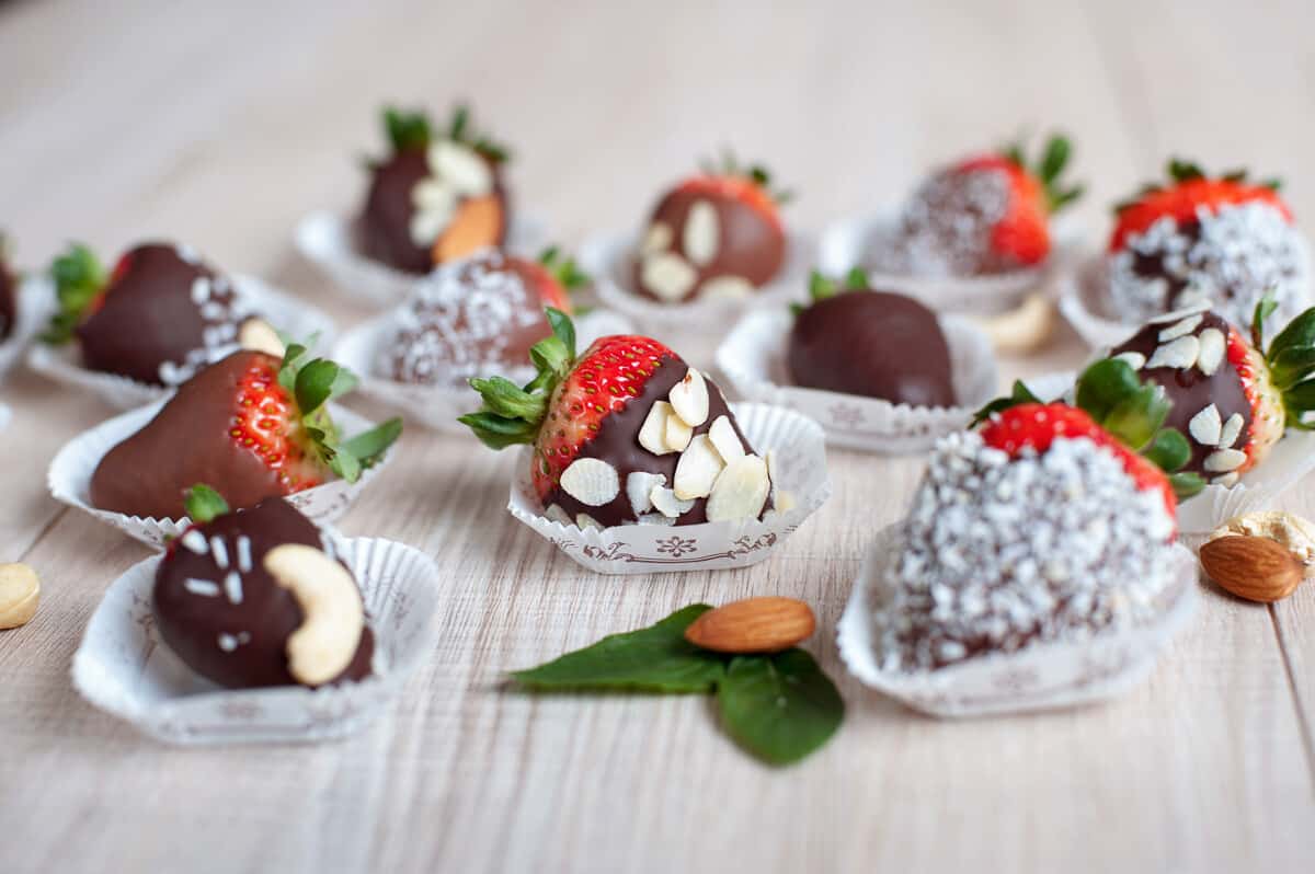 Chocolate covered strawberries in individual little paper cups. Chocolate strawberries have been dipped in sliced almonds and coconut.