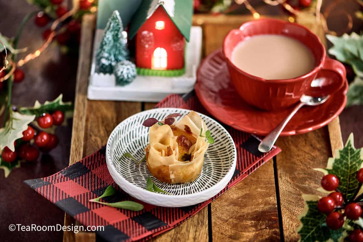 Grilled red pepper and asparagus mini quiche on little plate with cup of te and decorative mini house in the background