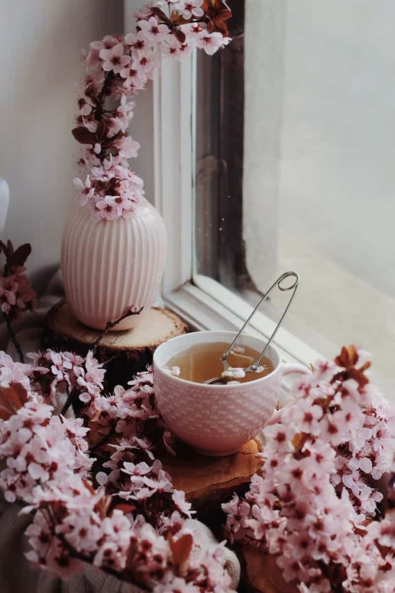 freshly brewed tea in cup among flowers on windowsill