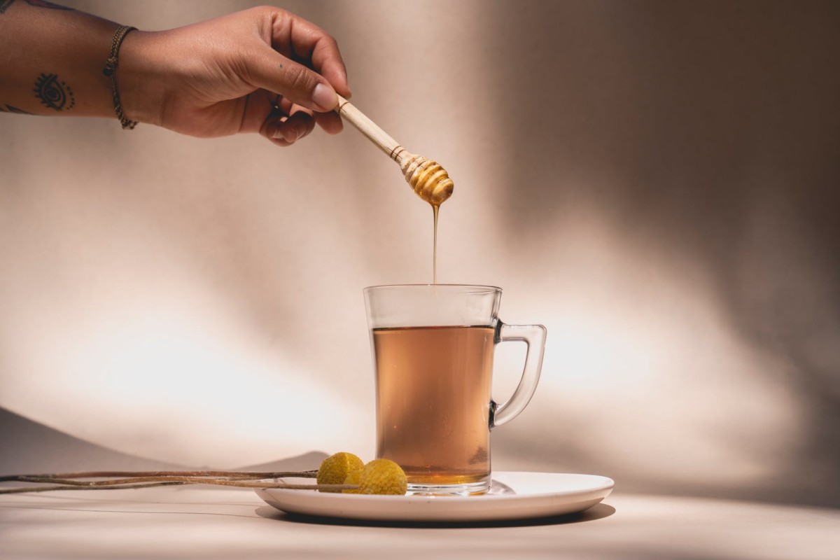 a person holding a honey dipper over a beverage